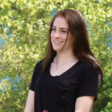 Decorative: A smiling student standing infront of a sun dappled tree.